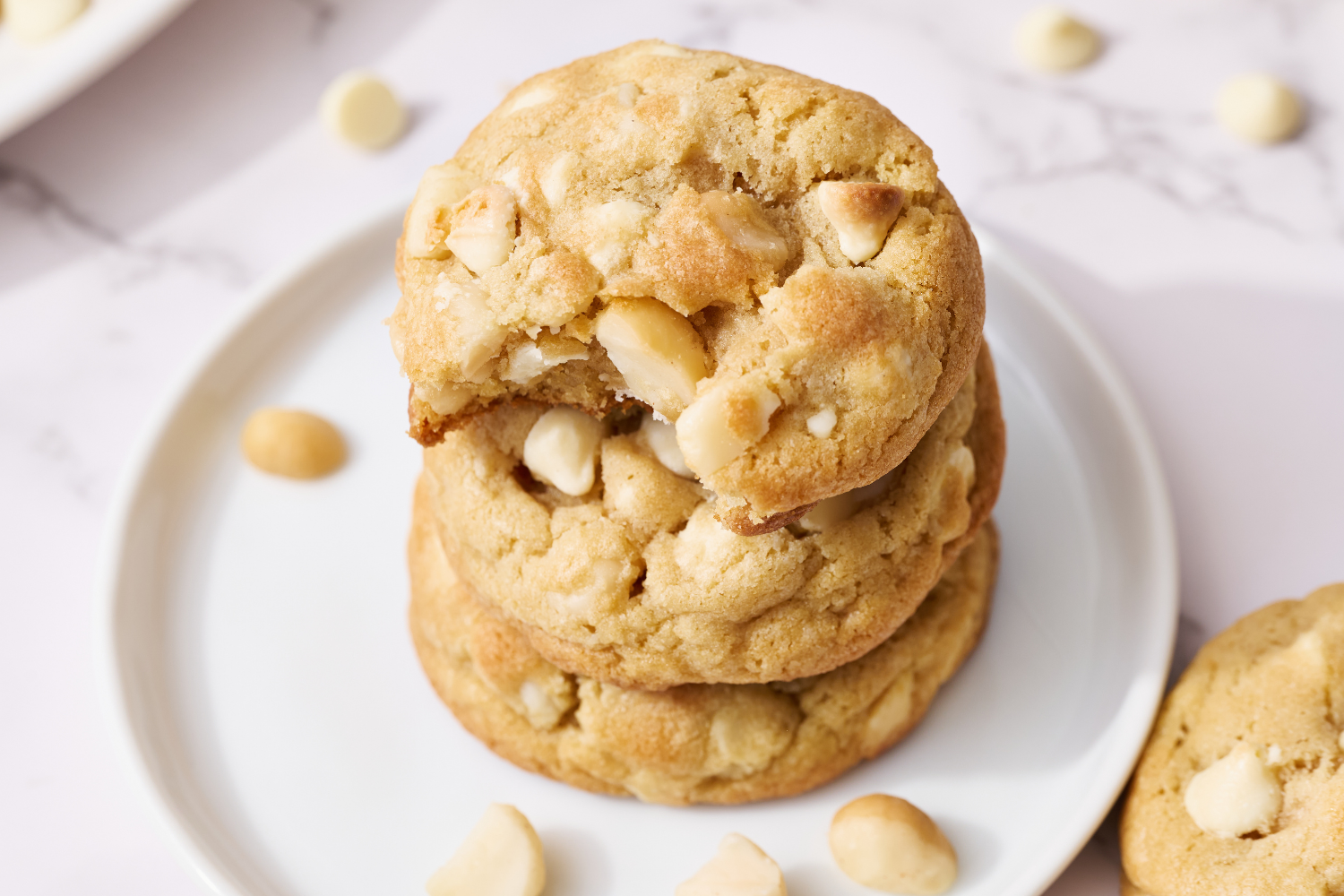 stack of White Chocolate Macadamia Nut Cookies, with the top cookie with a bite taken out.