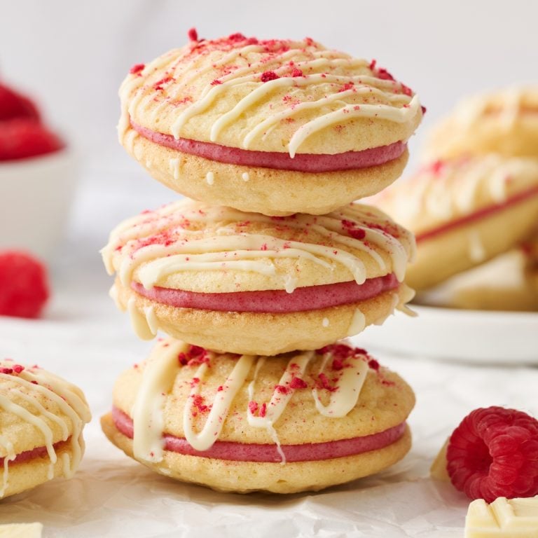a stack of three Raspberry Cream Sandwich Cookies, with some fresh raspberries nearby.