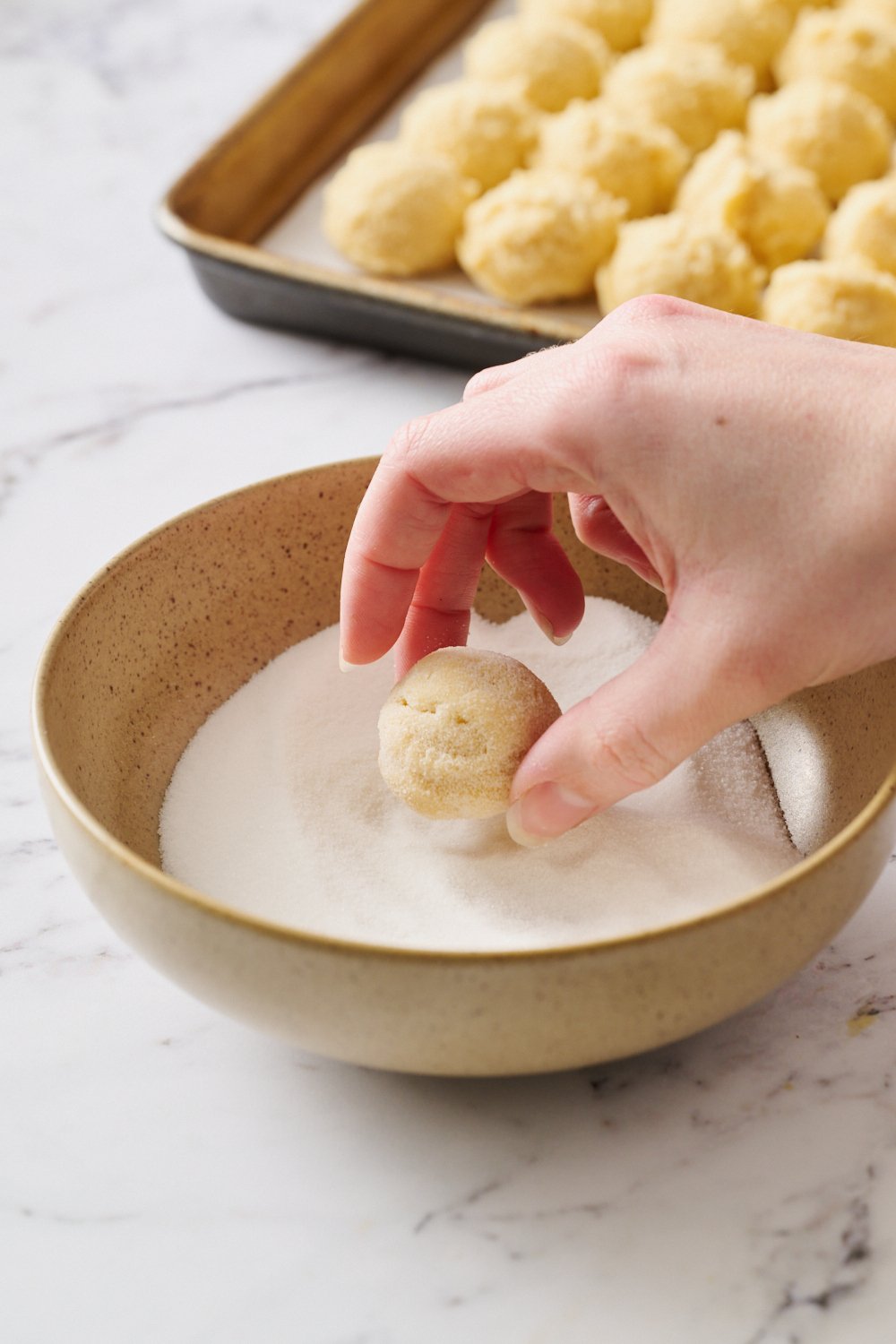 a cookie in a bowl of sugar being rolled to coat before baking.