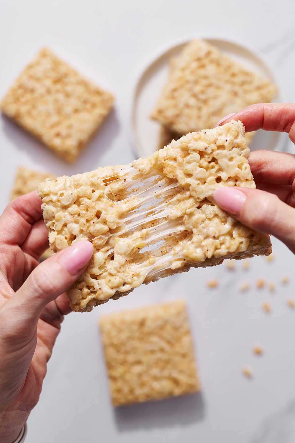 pulling a slice of Brown Butter Rice Crispy Treats apart to show the marshmallowy gooiness!