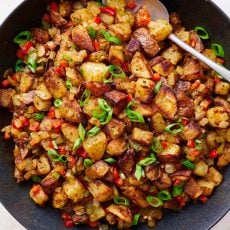 crispy home fries in a skillet with seasonings, veggies, and green onions.