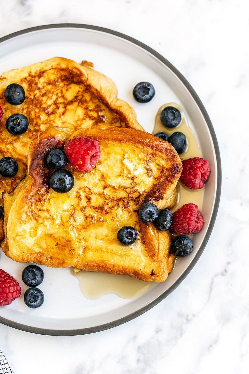 Two slices of French toast on a plate with maple syrup and berries