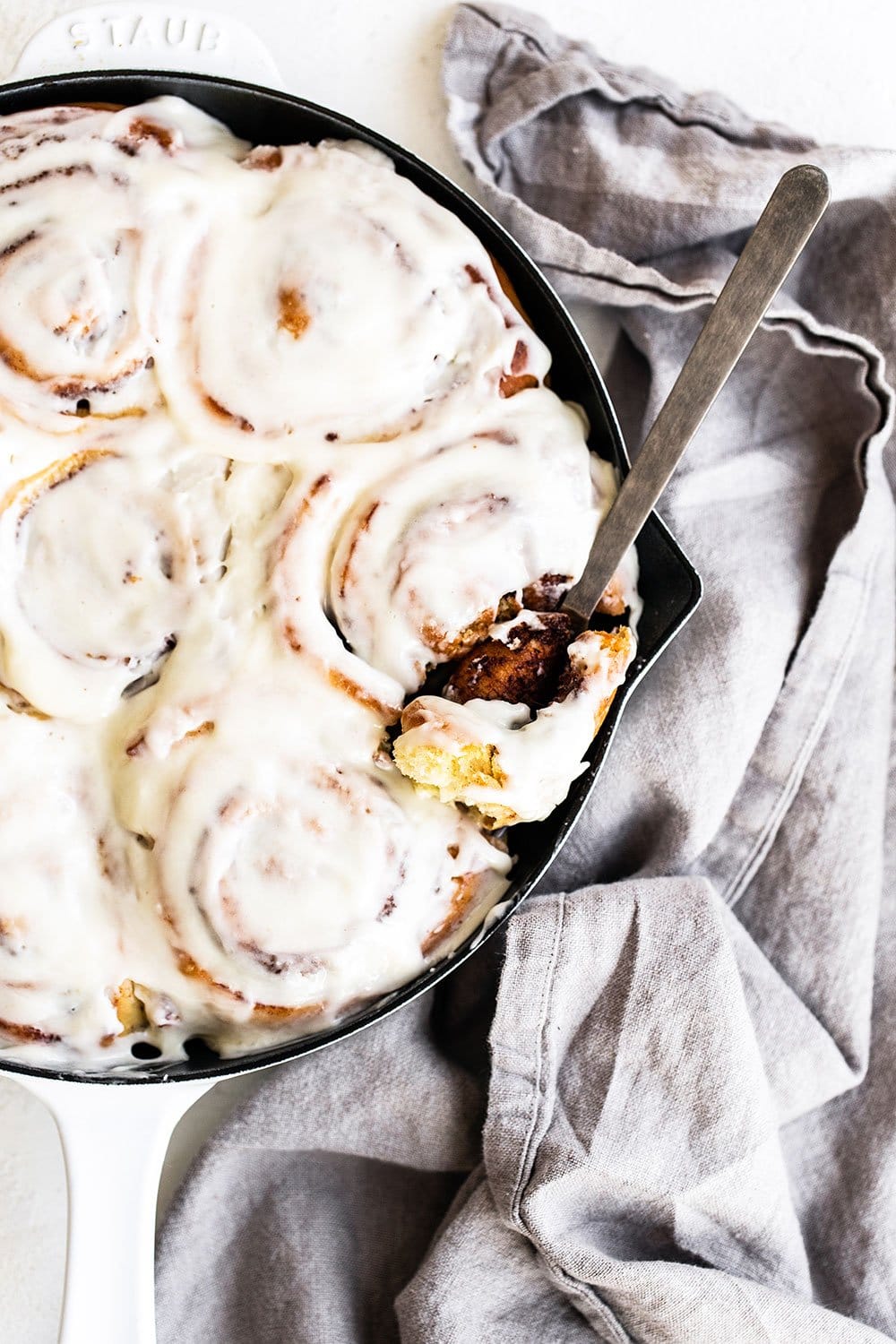 Cast iron pan with cinnamon buns and fork taking bite