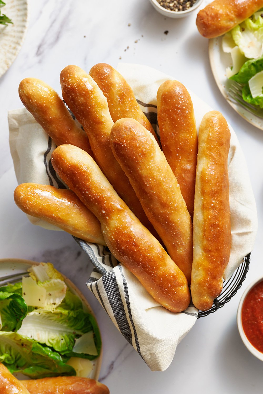 a batch of warm breadsticks wrapped in a blue and white towel, with a side salad in the background.