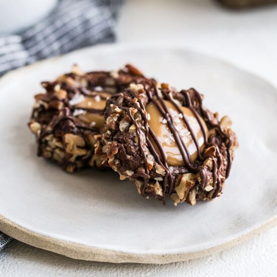 This Turtle Thumbprint Cookie recipe features a cocoa cookie rolled in pecans, filled with a salted caramel thumbprint, and drizzled with chocolate. A perfect Christmas cookie recipe!