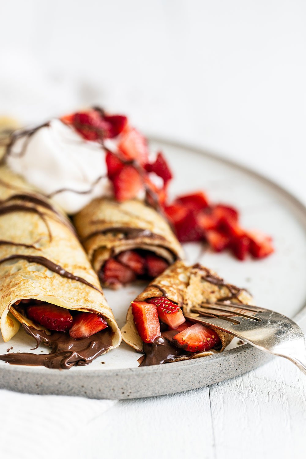 two rolled crepes stuffed with nutella and strawberries and topped with whipped cream