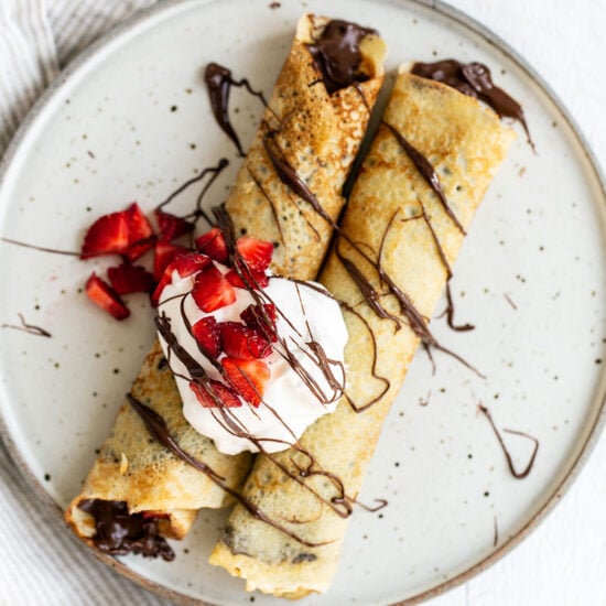 Two crepes on a plate with nutella, strawberries, and whipped cream on top