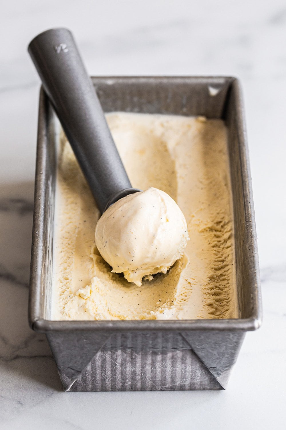 a loaf pan full of homemade French vanilla ice cream, with an ice cream scoop, ready to serve