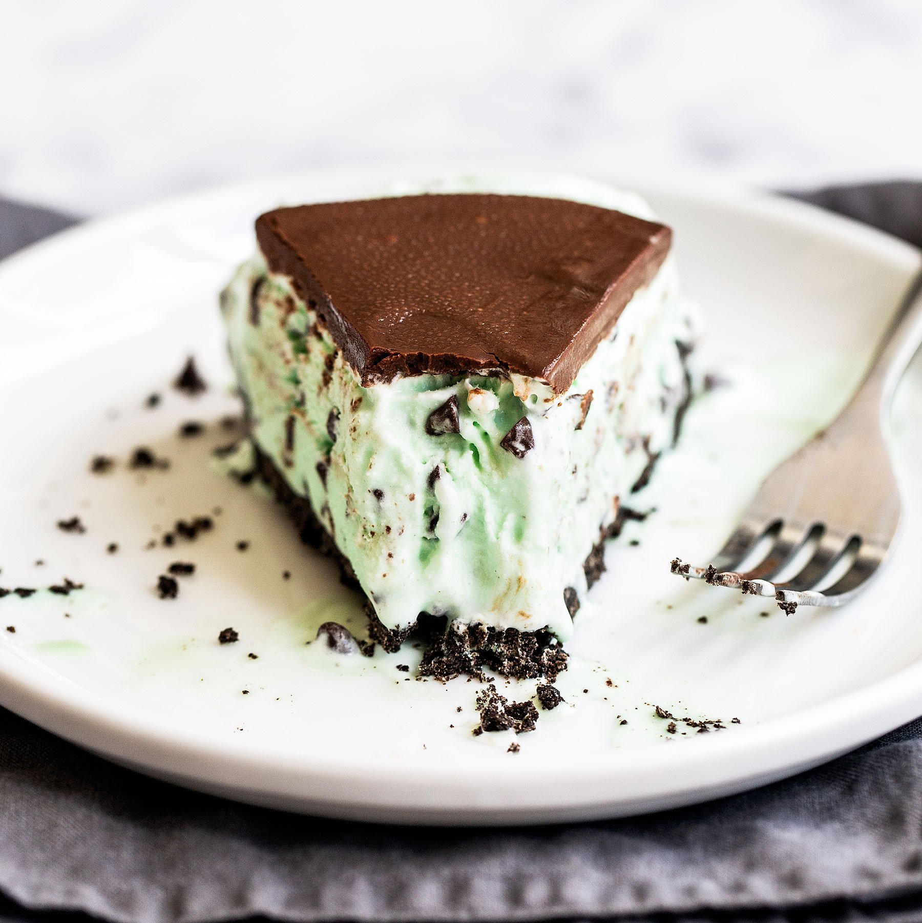 Slice of mint chocolate chip ice cream pie with Oreo crust and chocolate ganache on top