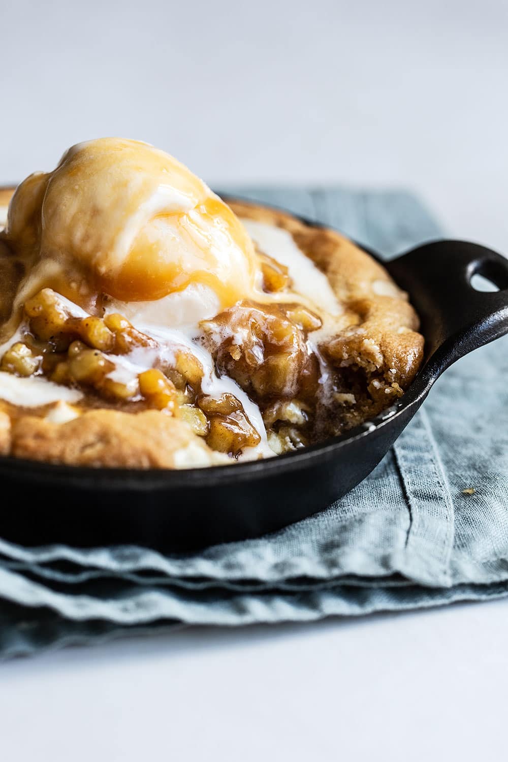A bite taken out of gooey white chocolate pizookie topped with apple pie filling, caramel, and ice cream