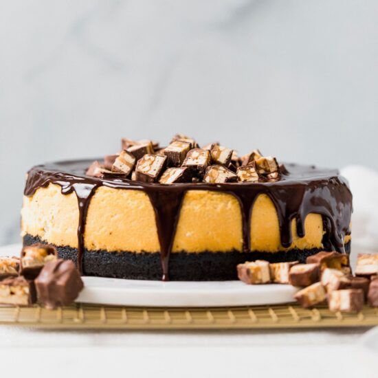 Decadent Snickers Cheesecake recipe with Oreo crust and chocolate ganache!