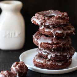 a stack of four doughnuts on a plate, with some donut holes beside it and a glass of milk in the background.