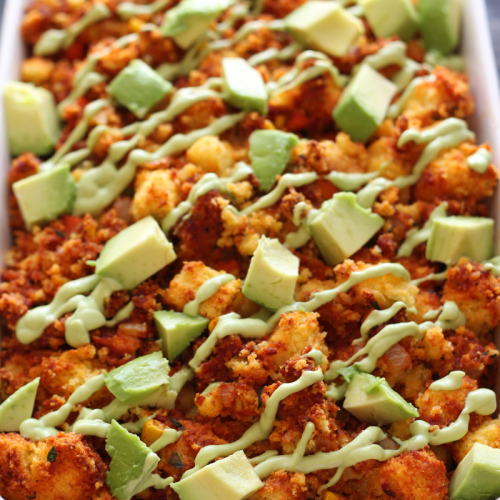 cornbread stuffing with chorizo, topped with crema and fresh diced avocado, in a ceramic dish.