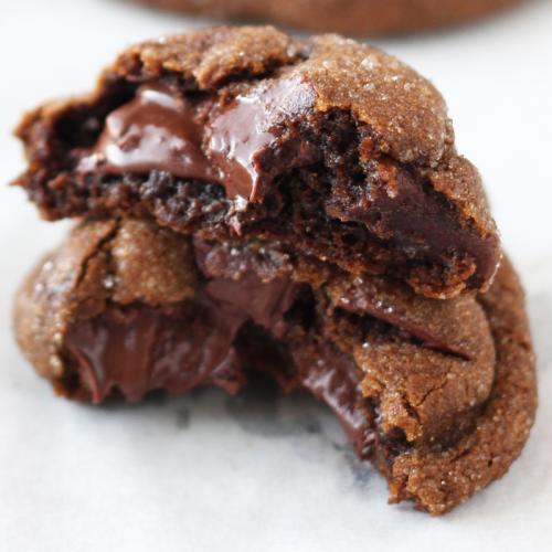 a chocolate gingerbread cookie torn in half and the two halves stacked, with gooey melty chocolate visible.
