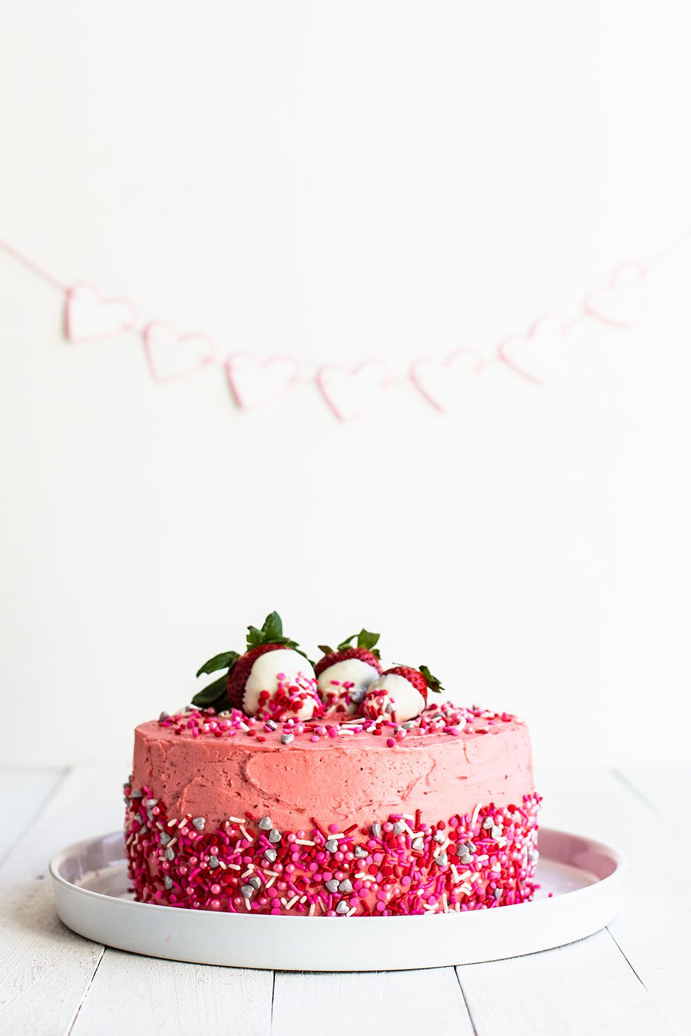 Pink strawberry frosted chocolate Valentine's Day cake on a plate with heart sprinkles