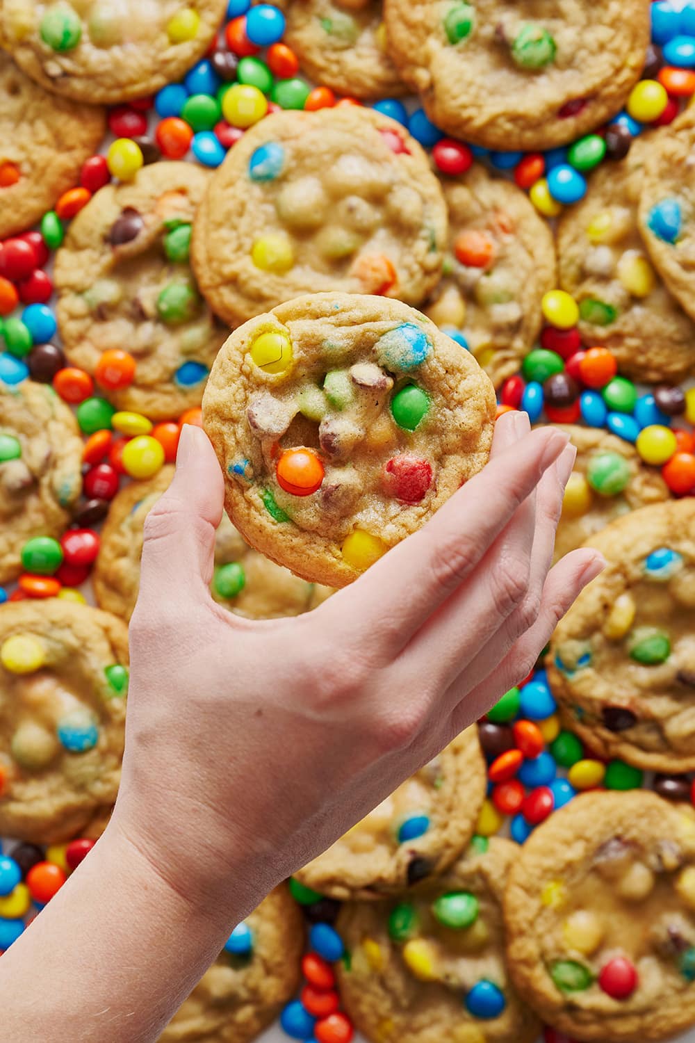 in an ocean of rainbow M&Ms, holding one soft and chewy M&M cookie
