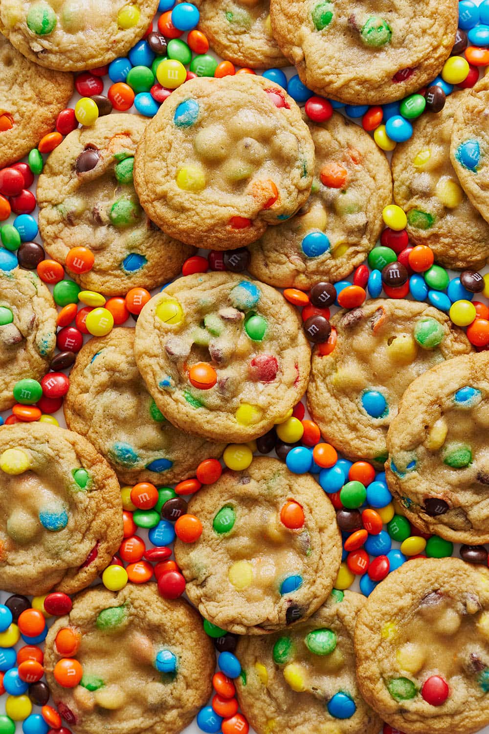 lots of soft and chewy M&M cookies with rainbow M&Ms scattered around