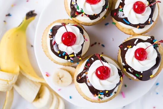 Banana cupcakes with vanilla buttercream frosting, chocolate ganache, sprinkles, whipped cream, and a cherry on top.