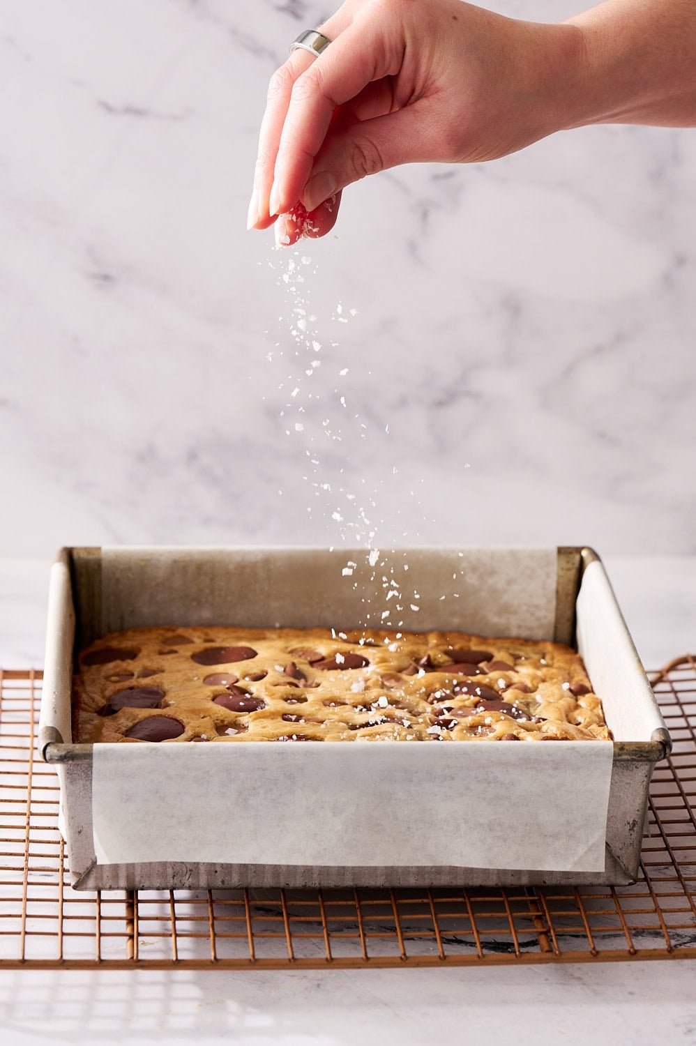action shot of sprinkling flaky sea salt onto tray of freshly baked blondies