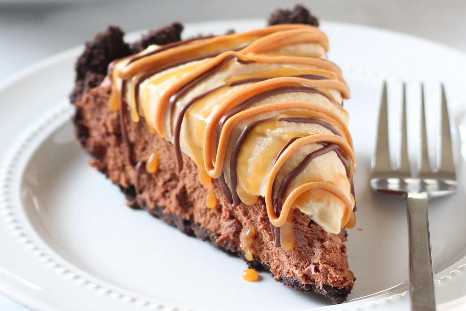 a slice of Chocolate Peanut Butter Caramel Mousse Pie with drizzled peanut butter, caramel and melted chocolate on top, ready to serve