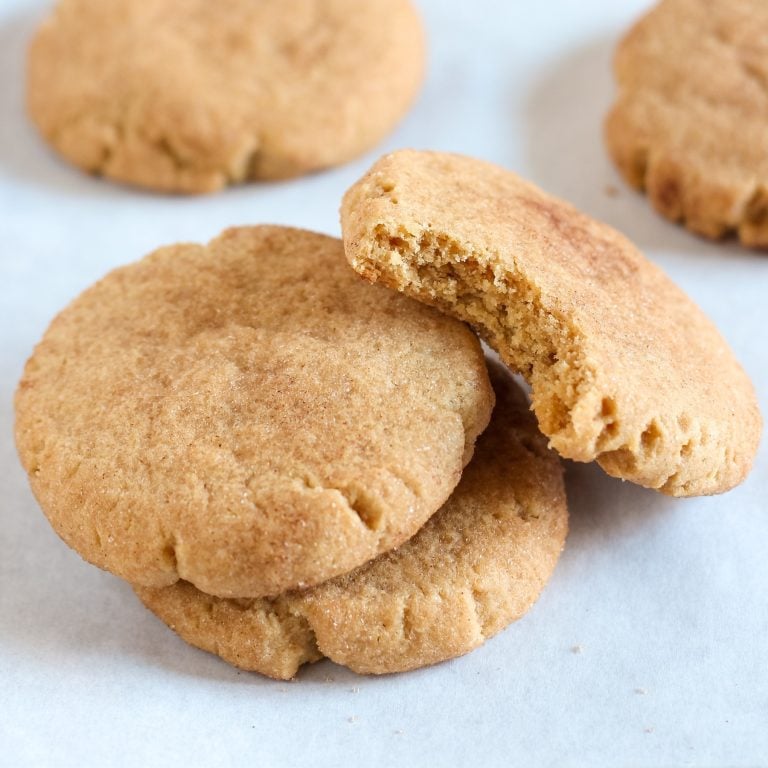 three peanut butter snickerdoodles stacked on white parchment paper.