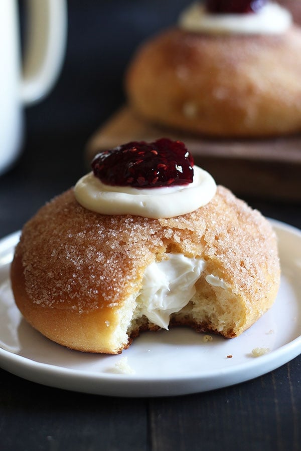 Cheesecake Stuffed Baked Doughnuts feature a fluffy yeast-raised baked doughnut coated in cinnamon sugar, stuffed with sweetened cream cheese, and topped with a dollop of raspberry jam.