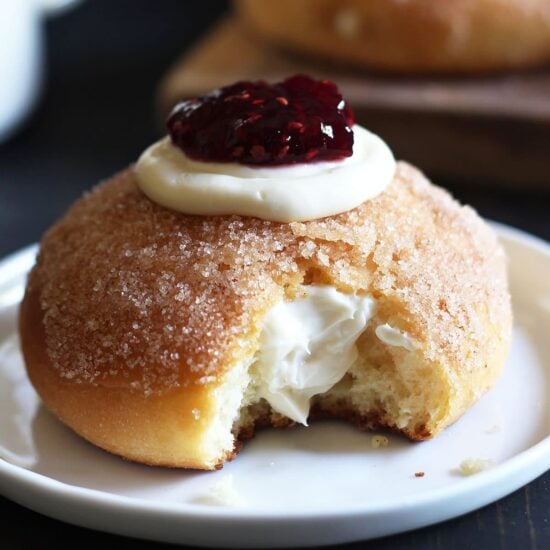 Cheesecake Stuffed Baked Doughnuts feature a fluffy yeast-raised baked doughnut coated in cinnamon sugar, stuffed with sweetened cream cheese, and topped with a dollop of raspberry jam.