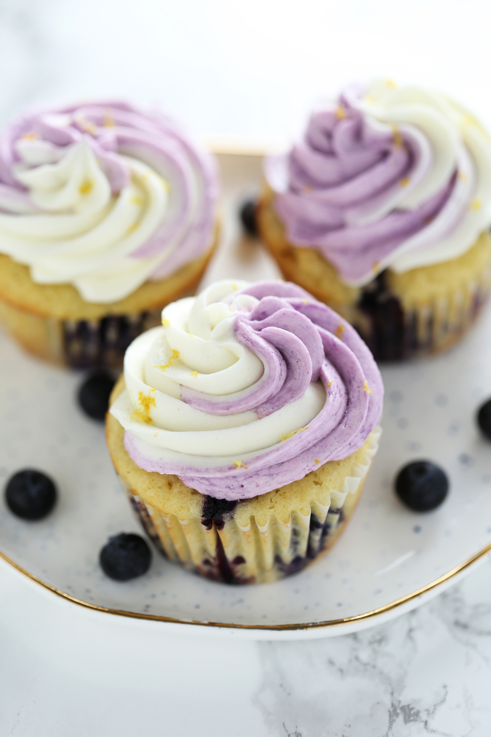 three lemon blueberry cupcakes, topped with buttercream frosting, sprinkled with a little lemon zest.
