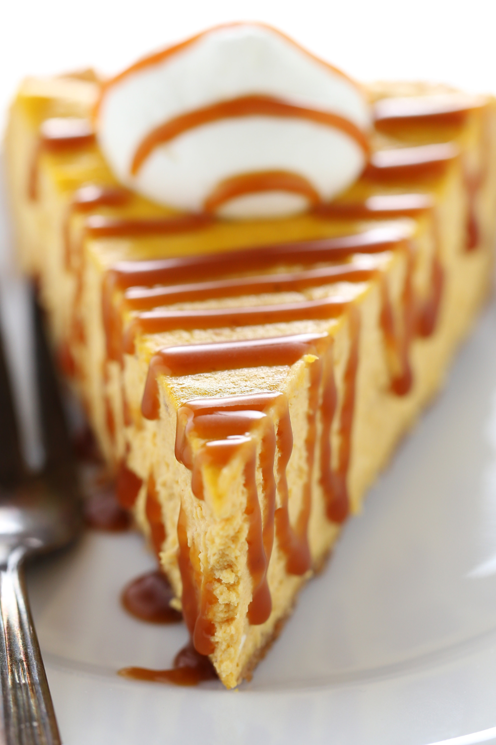 a slice of pumpkin caramel cheesecake, drizzled with salted caramel sauce and topped with a dollop of whipped cream