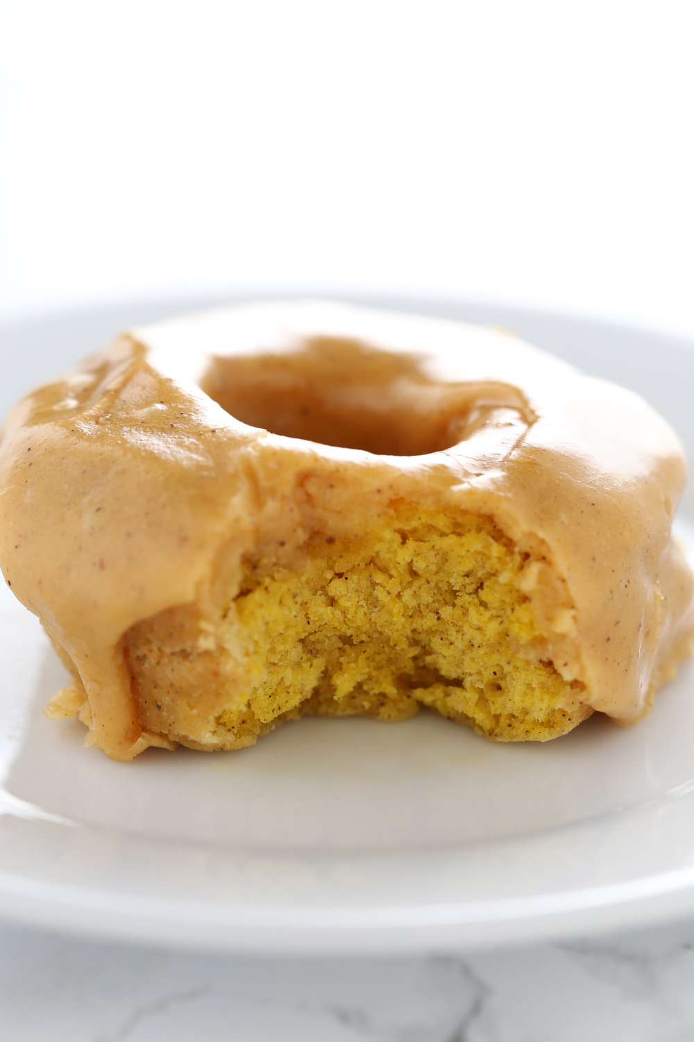 pumpkin donut topped with thick shiny pumpkin spice glaze, with a bite taken out