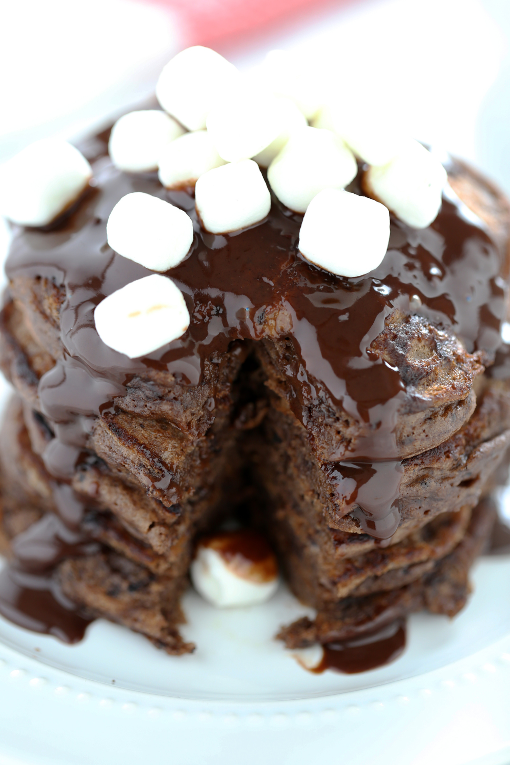 a stack of hot chocolate pancakes with fudge and mini marshmallows on top, with a slice taken out.