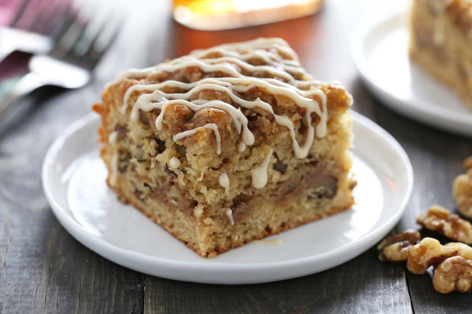 slice of maple coffee cake on a plate, surrounded by walnuts and drizzled with a simple maple icing