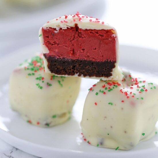 Red Velvet Cheesecake Bites feature squares of homemade red velvet cheesecake dipped in white chocolate and garnished with festive holiday sprinkles! Perfect Christmas treat.