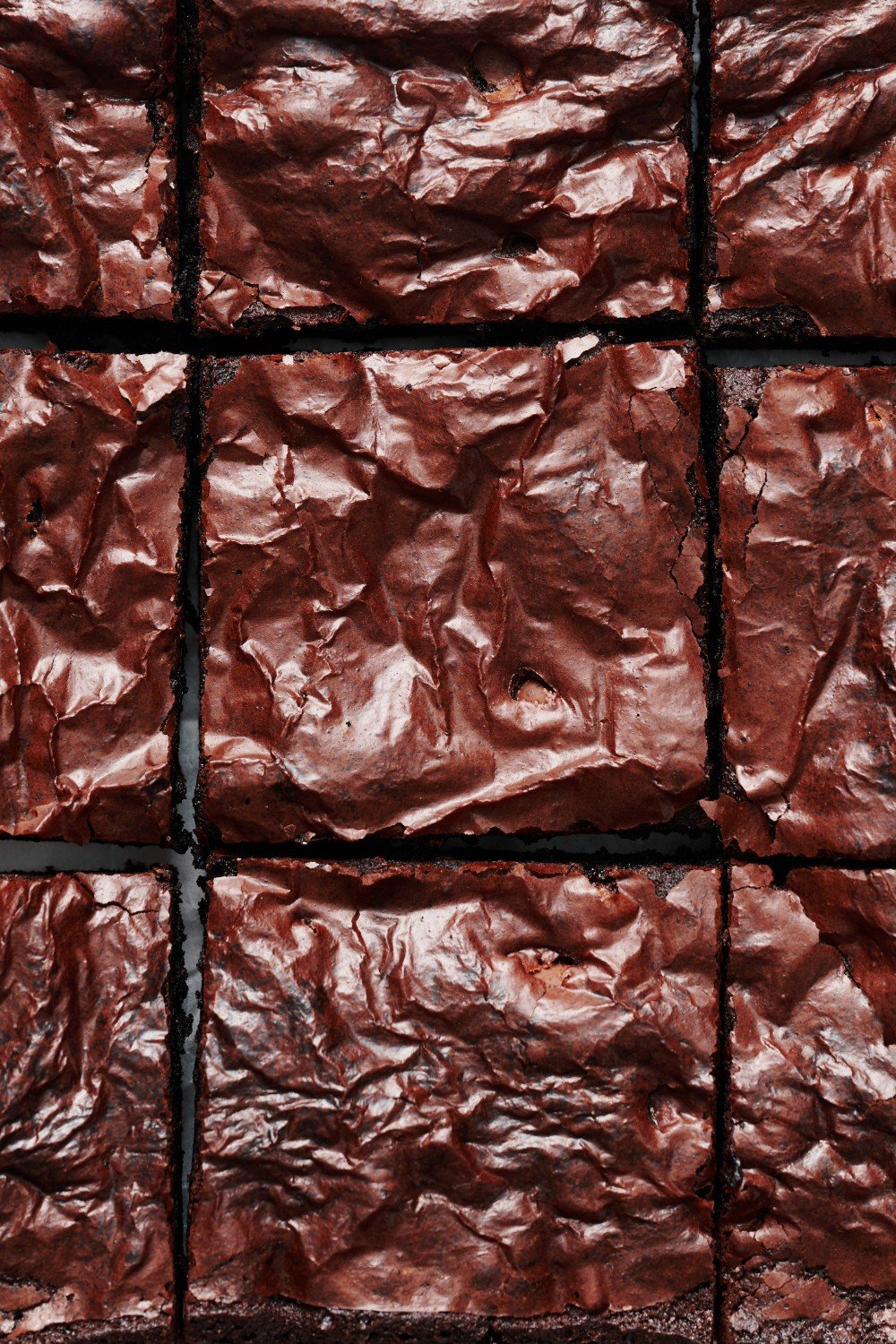 a whole pan of baked sliced brownies from above, showing their shiny thin crust. 