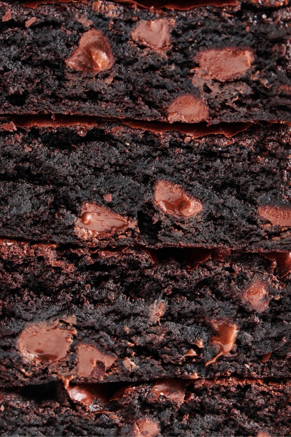 closeup of a stack of brownie slices, showing their dark chocolate color, chocolate chips, and fudgy chewy texture.