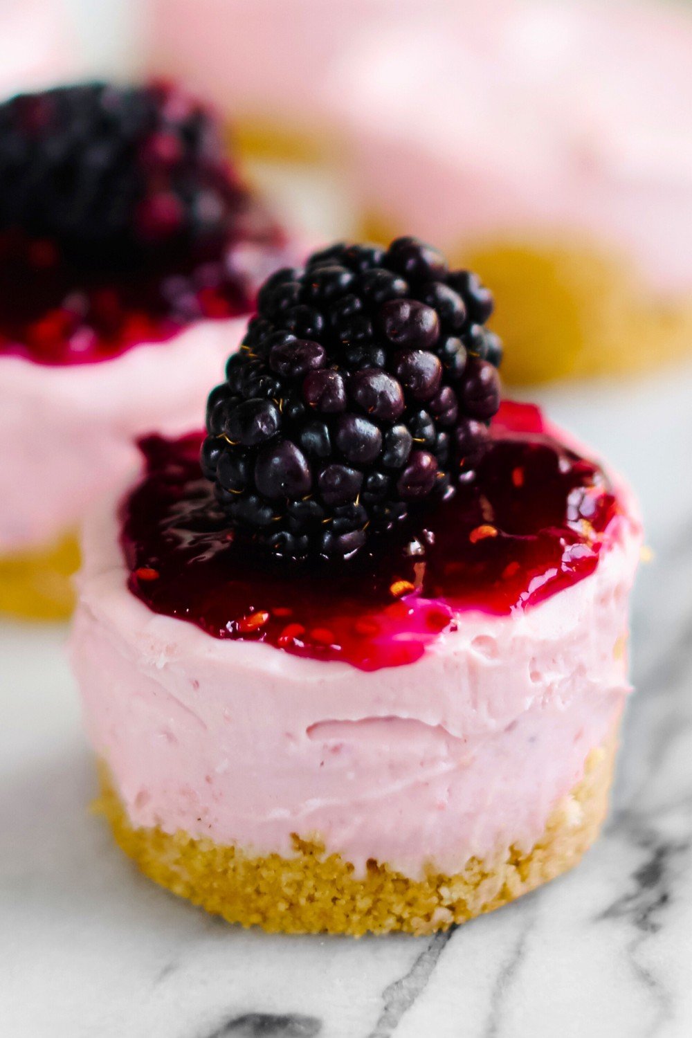 mini cheesecake topped with a blackberry sauce, garnished with a fresh blackberry on top.