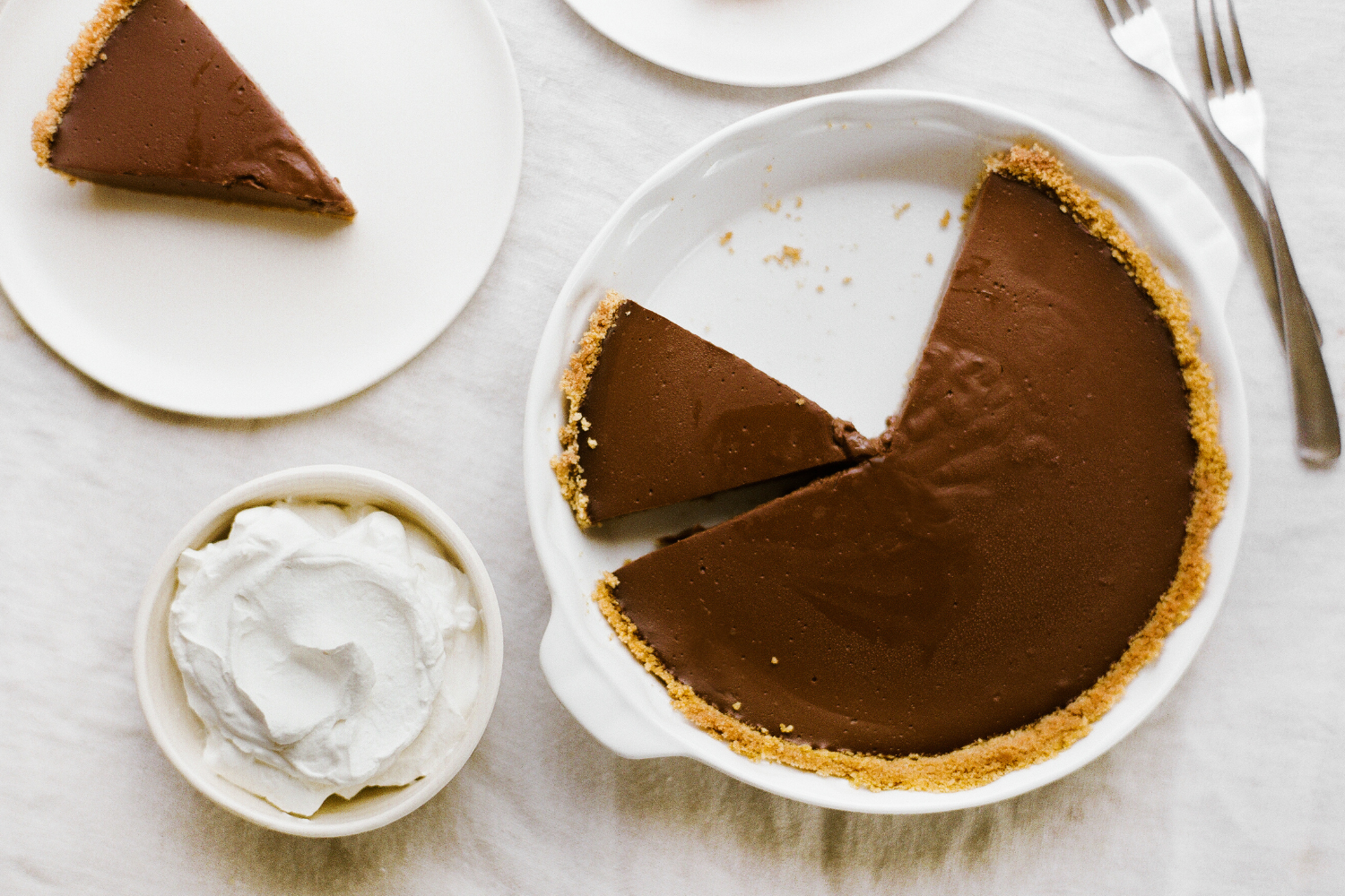 a whole chocolate pudding pie with a slice removed, with whipped cream on the side