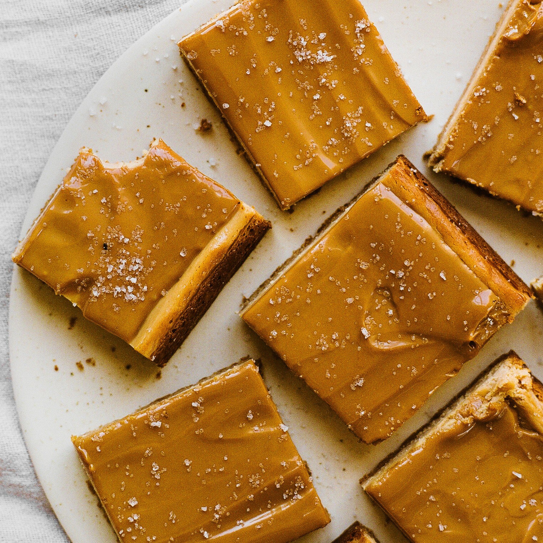 several dulce de leche cheesecake bars on a white plate, ready to serve.