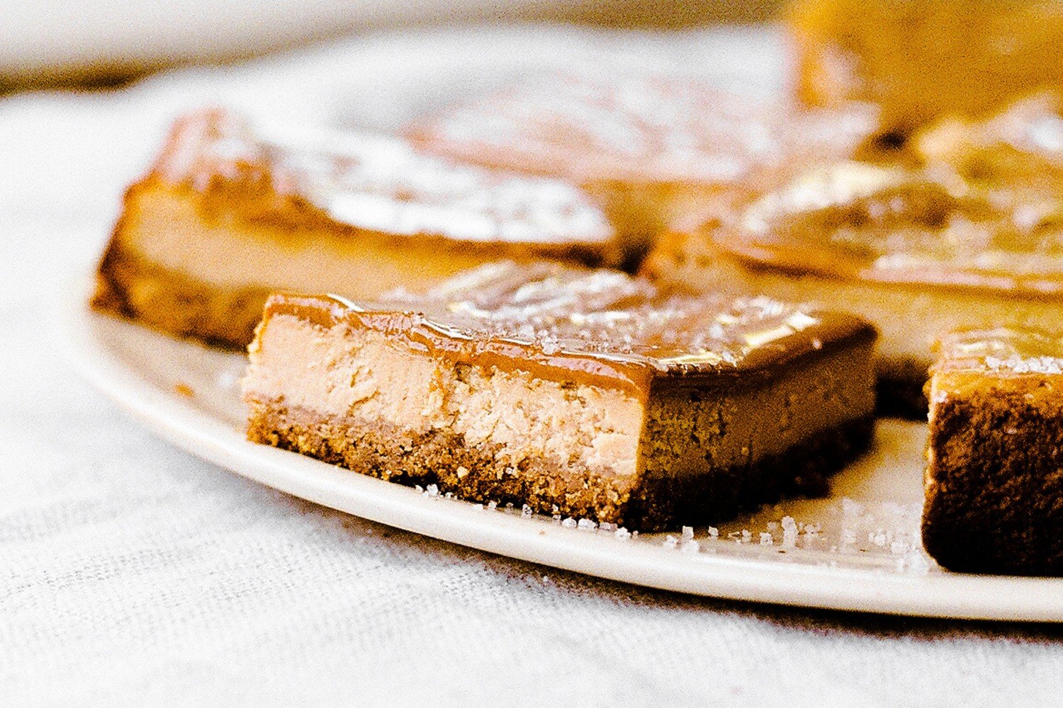 cheesecake bars topped with sauce and sprinkled with flaky sea salt, on a white plate.