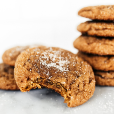 a thick gingerdoodle cookie with a bite taken out, with more whole cookies stacked in the background.