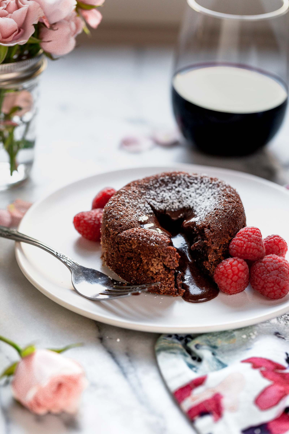 a chocolate lava cake on a white plate with a fork and some fresh raspberries.