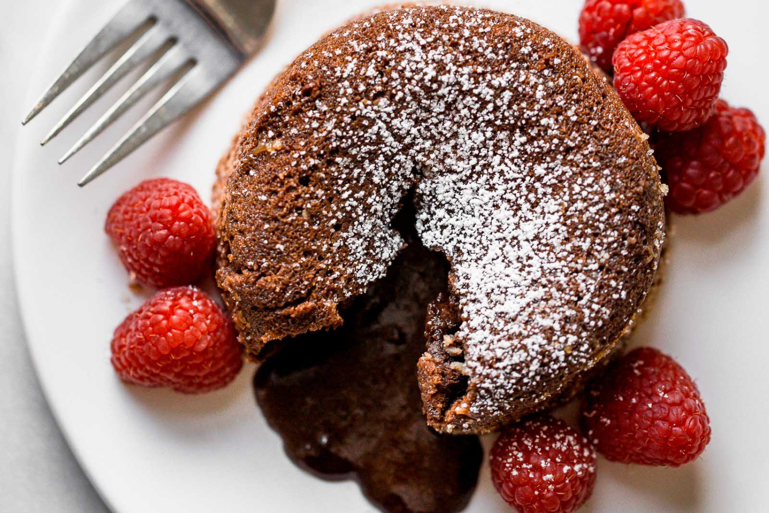 one Chocolate Lava Cake on a plate, broken open so the molten filling pours out.