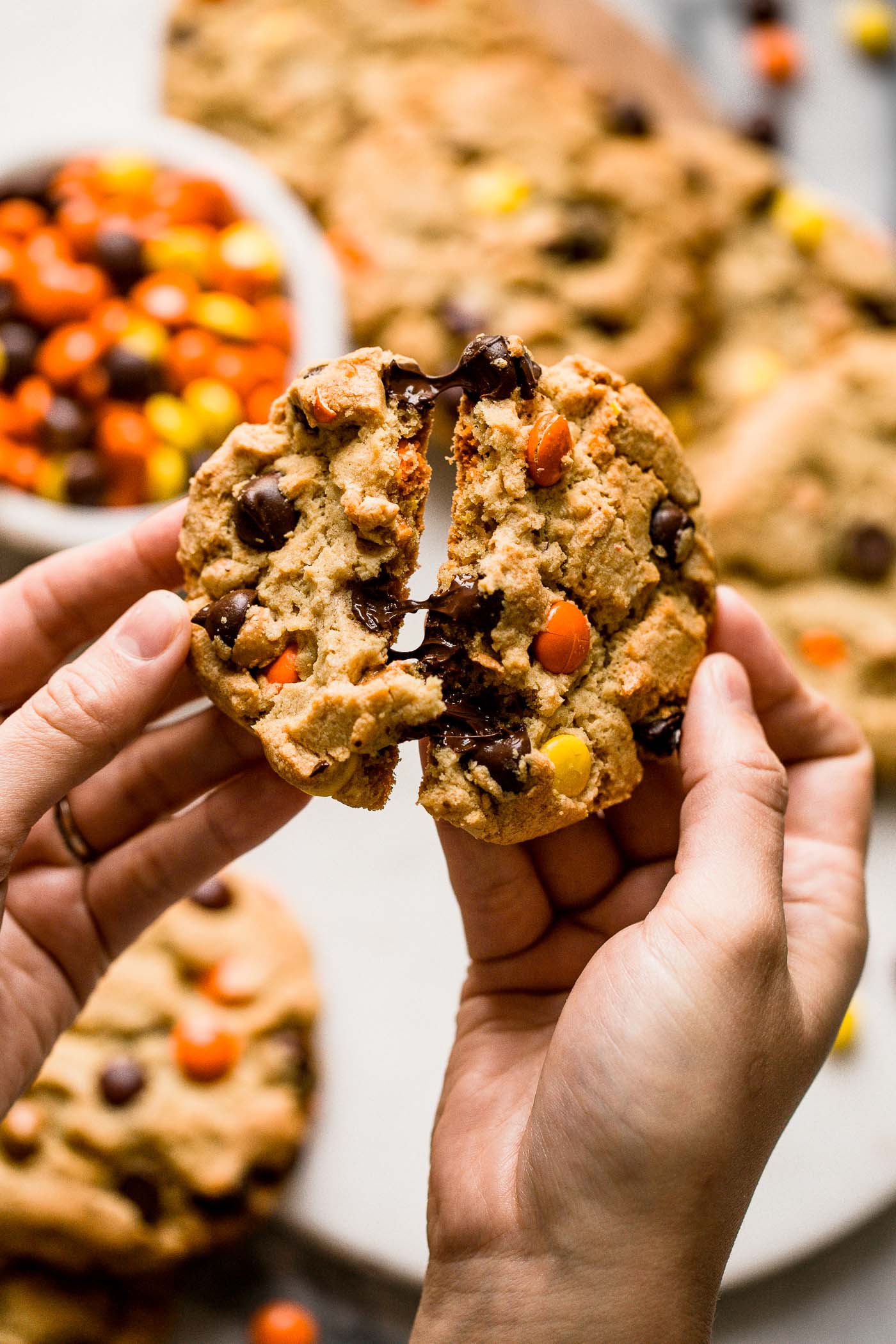 giant peanut butter chocolate chip cookie broken in half with Reese's Pieces and more cookies in the background