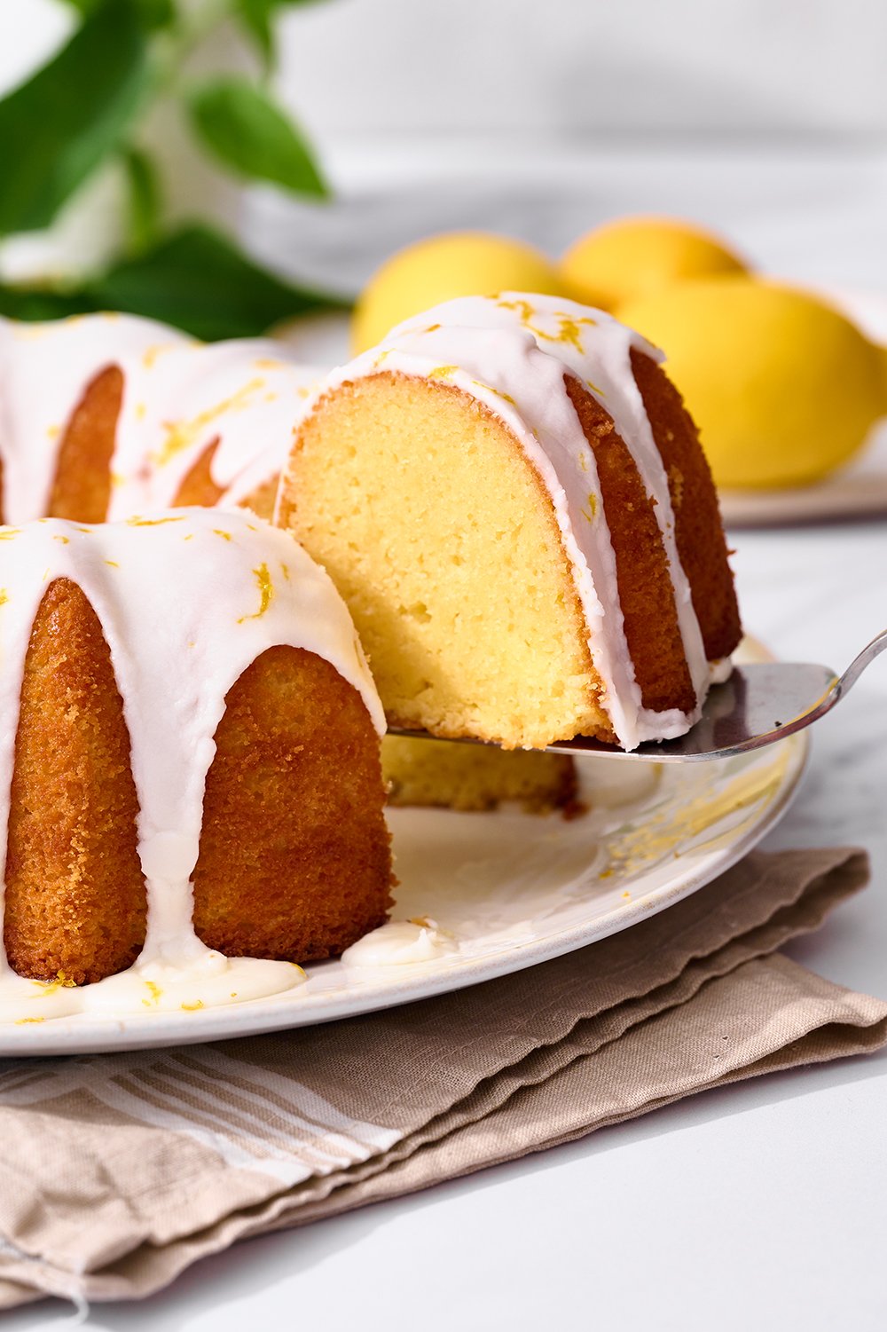 serving spoon lifting a slice of easy lemon bundt cake recipe off of platter, ready to serve for Easter dessert