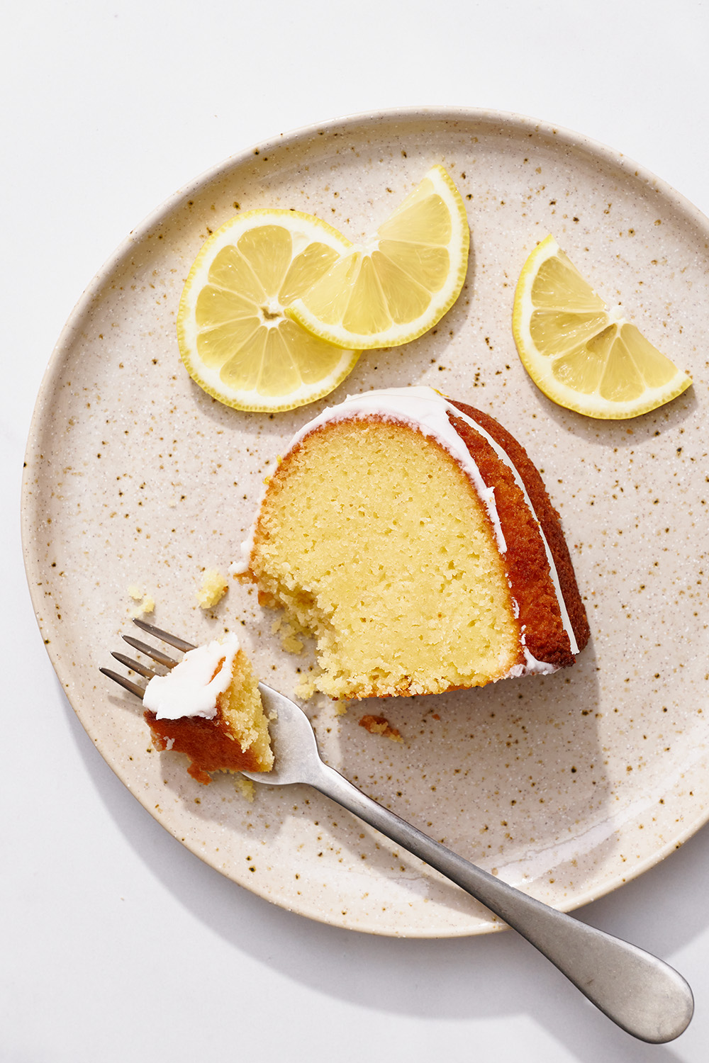 slice of lemon bundt cake on a plate with a fork and a bite ready to eat