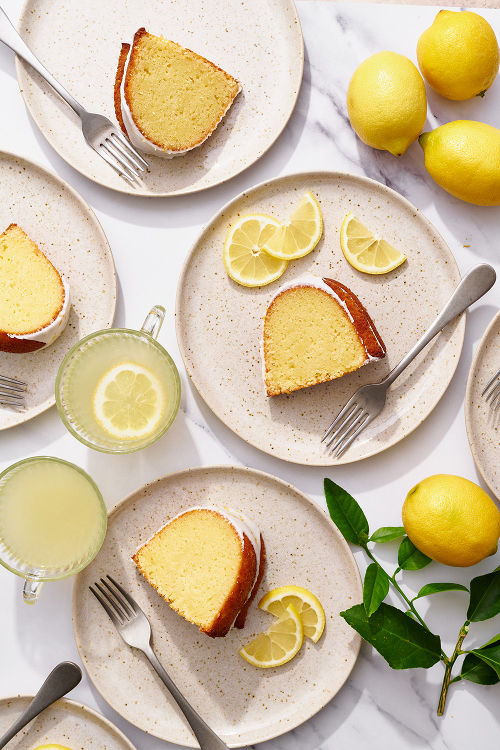 Slices of lemon bundt cake on plates with forks and slices of fresh lemons