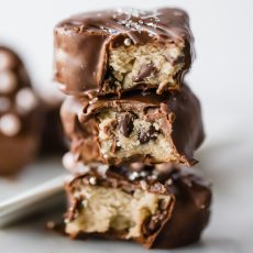 three cookie dough hearts covered in chocolate, stacked on top of each other, each with a bite taken out to show the insides.