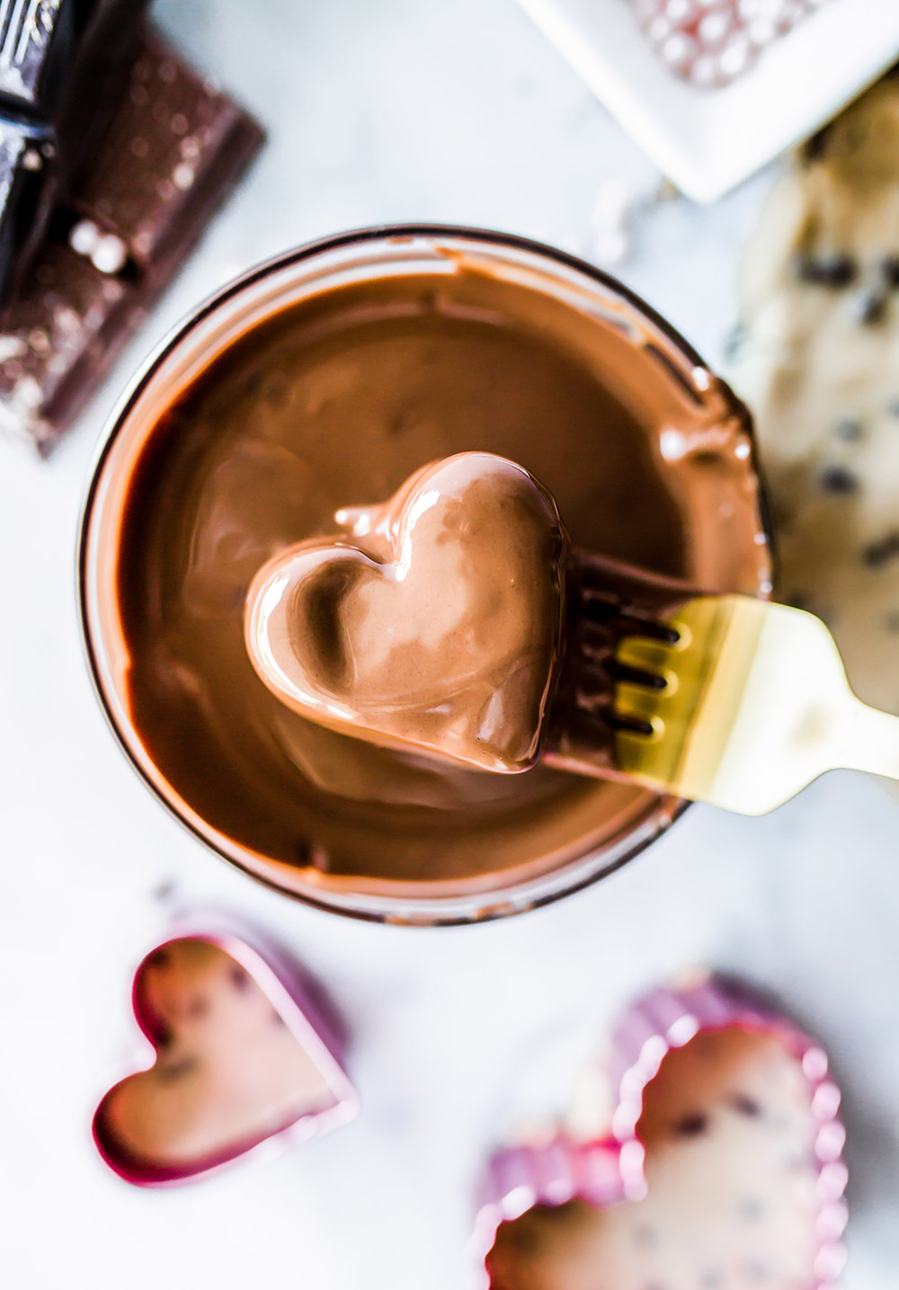 a cookie dough heart being dipped in a small bowl of melted chocolate.