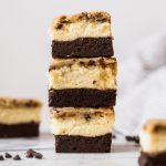 bars with brownie, cheesecake and cookie dough layers, stacked three high on a marble surface