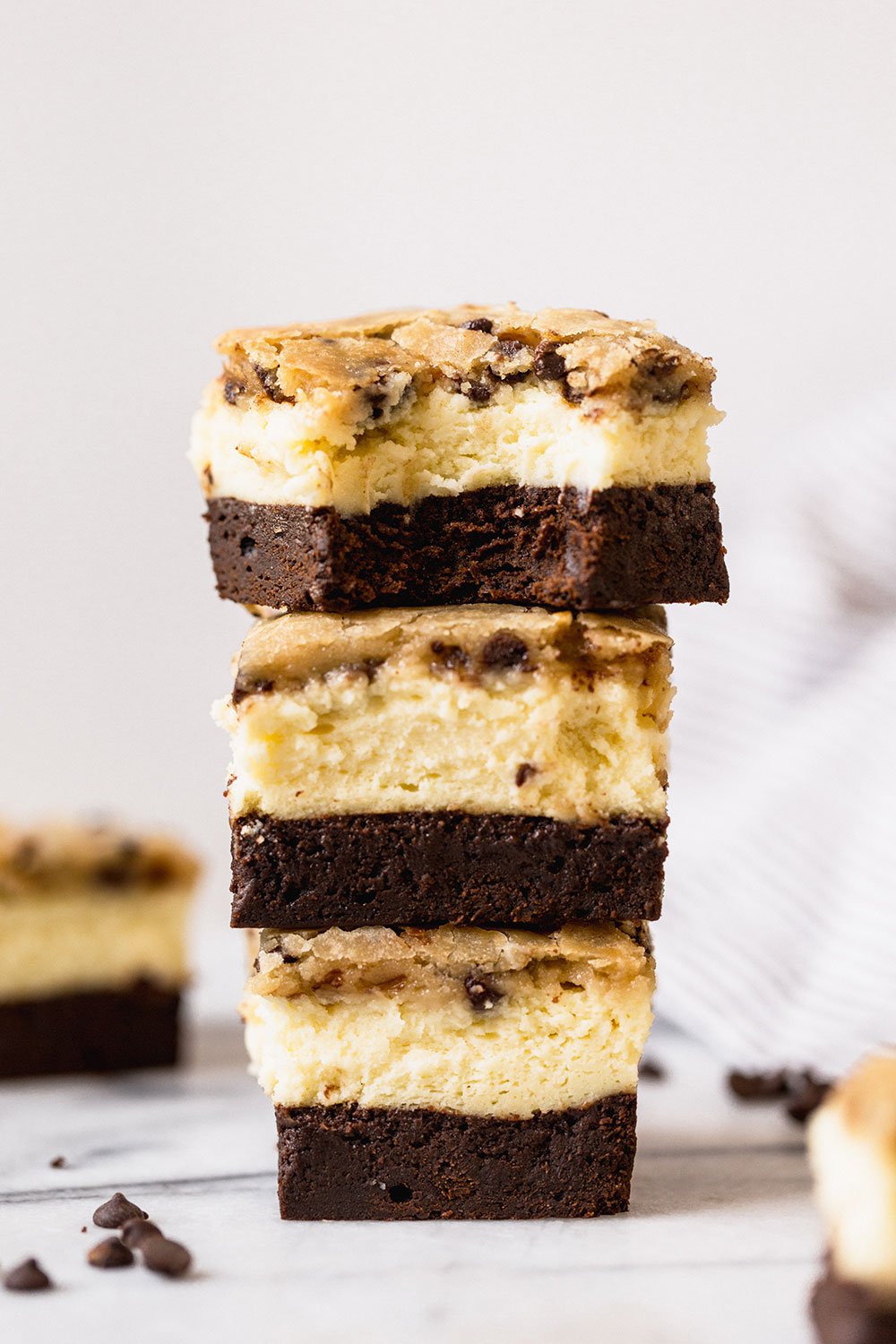 three Brownie Bottom Cookie Dough Cheesecake bars, stacked on top of each other